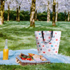 A large cooler tote bag in white with colourful nautical patterns, alongside a picnic spread and a drink bottle.