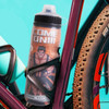 A drink bottle with a double wall design, featuring a graphic on its surface, placed in a bike holder. Predominantly orange and black.