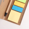 A ruler sticky note pad with a pen features yellow, blue, green, and orange sticky notes on a brown background.
