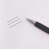 A black barrel ball pen lies beside three lines drawn on a sheet of paper. The pen features a silver tip and grip.