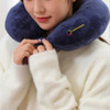 A U-shaped travel pillow in navy blue, featuring a logo, being adjusted by a person wearing a light sweater.
