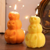 Triple pumpkin-shaped candles in orange and yellow, featuring carved skull designs, with flames flickering from the tops.