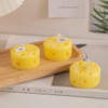 Round cheese-shaped candles in yellow, featuring holes, placed on a wooden serving tray.
