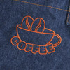 A denim apron featuring an orange embroidered design of a coffee cup with coffee beans.