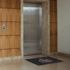 A nylon floor mat in front of a sleek elevator, featuring a logo and multicoloured text on a dark background.