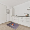 A rectangular diatomite mat in grey with a logo, placed on a wooden kitchen floor.