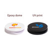 A round phone holder in white and black, featuring an epoxy dome and UV print, with a logo on each.