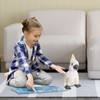 A child with a plaid shirt sits on a rug, holding a game board, next to a white and yellow cockatoo plush toy.