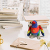 A colourful plush lorikeet toy with blue wings and a red breast, placed among books and stationery on a table.