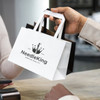 A small flat handle paper bag featuring a black and white design, held by a person at a counter.