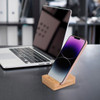 A bamboo phone holder features a sleek design with a pink phone displayed beside a laptop. The product has a logo.
