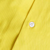 A close-up of a yellow cotton shirt featuring a white button, highlighting its fabric texture.