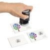 A self-inking stamp in black is being pressed onto white cards featuring a colourful tree design and a logo.