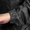 A close-up view of a black windbreaker sleeve with an elastic cuff. The jacket is lightweight and smooth in texture.