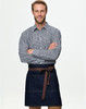 A man in a checkered shirt wears a denim half apron with a brown tie belt. The apron features pockets and a logo.