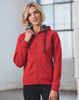 A red full zip fleece hoodie with a grey hood, featuring a logo, posed by a model in a bright interior setting.