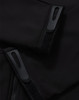 Close-up of a black softshell jacket featuring zippers and velcro details. The jacket has a logo on it.