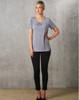 A grey short-sleeve knit top with pleats, paired with black fitted pants, worn by a model against a textured background.