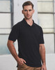 A man in a black polo shirt stands against an industrial background, featuring short sleeves and a standard collar.