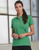 A green women's polo shirt with a fitted design, featuring a collar and buttons, displayed by a model in an industrial setting.