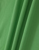 A close-up of a green, textured fabric featuring folds, suitable for polo shirts. It has a branding logo.