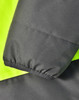 A close-up of a two-tone safety jacket featuring fluorescent yellow and charcoal grey fabric. It has a textured finish and elastic cuffs.