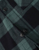 A close-up of a black and green flannel plaid shirt featuring button details. The shirt has a classic check pattern.