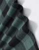 A close-up of a unisex flannel shirt in black and green plaid fabric, featuring a logo.