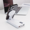 A white power bank with a phone attached, featuring multiple USB ports and a sleek design, placed on a desk with a laptop.