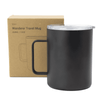 A travel mug in matte black with a clear lid, next to a cardboard box featuring a logo.