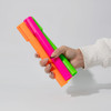 A hand holding three jumbo highlighters in vibrant neon pink, green, and orange colours, featuring a logo.