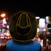 A person wearing a yellow and black striped straw hat with illuminated edges, set against a night-time background.