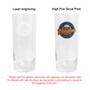 A tall, clear beer glass featuring a logo on one side and a laser-engraved design on the other.