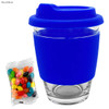 A royal blue glass coffee cup with a silicone lid and sleeve, accompanied by a packet of colourful jelly beans.