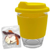 A reusable glass coffee cup with a yellow silicone lid and sleeve, accompanied by a clear bag of assorted jelly sweets.