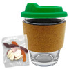 A glass coffee cup with a green lid and cork band, accompanied by a pack of mixed lollies in assorted colours.