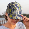 A cap featuring a tropical pattern with surfboards and palm trees in shades of green and yellow. It has a logo.