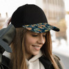 A black cap with a patterned peak, worn by a smiling woman outdoors. The cap features a vibrant design on the brim.