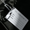 A black imprinted mini luggage tag featuring a blank white information card for name, phone, and address.