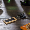 A rectangular bamboo keyring with a black surface, attached to a set of keys resting on a wooden surface.