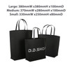 A set of three black boutique paper bags of varying sizes, featuring two handles and one with a logo.