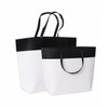 A small black and white paper bag with a black top and white bottom, featuring sturdy handles.