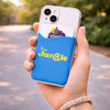 A blue phone wallet with a card slot, positioned on a hand, set against a blurred outdoor background.