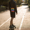 A cross body bag featuring a vibrant rainbow design is worn by a person on a skateboard in an outdoor setting.