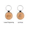 A round wooden keyring featuring a silver metal keyring attachment and two engraved designs on the wooden surface.