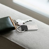 A silver metal keyring with a black PU leather detail, holding a key and a flash drive, resting on a grey surface.