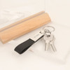 A PU leather keyring in black with a metal tag, holding two silver keys and displayed with a wooden block.