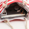 A tote bag with red and white stripes featuring a rope handle, containing a phone, sunglasses, and a catalogue.