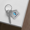 A silver house-shaped metal keyring attached to a key, with a logo on the keyring.