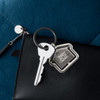 A silver metal keyring shaped like a house with a circular attachment, resting on a black wallet.